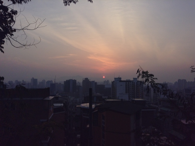 The sun rises over Seoul's mountains and buildings. 
